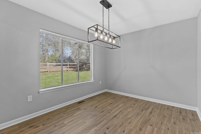 unfurnished dining area with a chandelier, hardwood / wood-style floors, and a textured ceiling