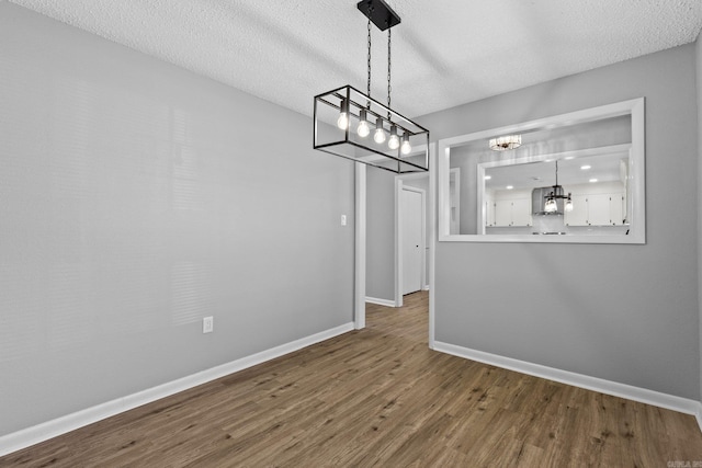 unfurnished dining area featuring hardwood / wood-style floors, a textured ceiling, and a chandelier