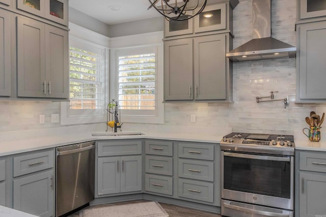 kitchen with tasteful backsplash, wall chimney exhaust hood, stainless steel appliances, sink, and pendant lighting