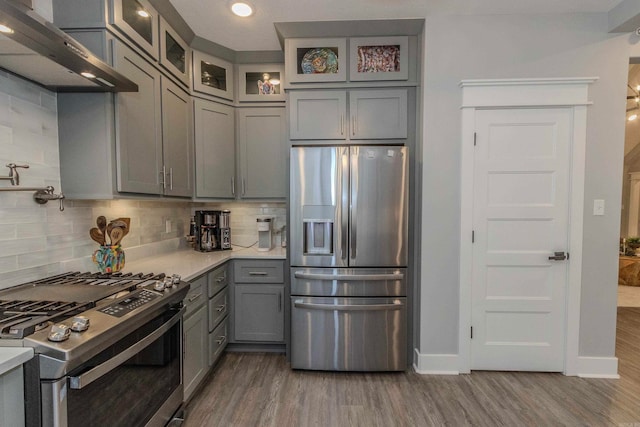 kitchen with tasteful backsplash, gray cabinetry, stainless steel appliances, dark hardwood / wood-style floors, and range hood