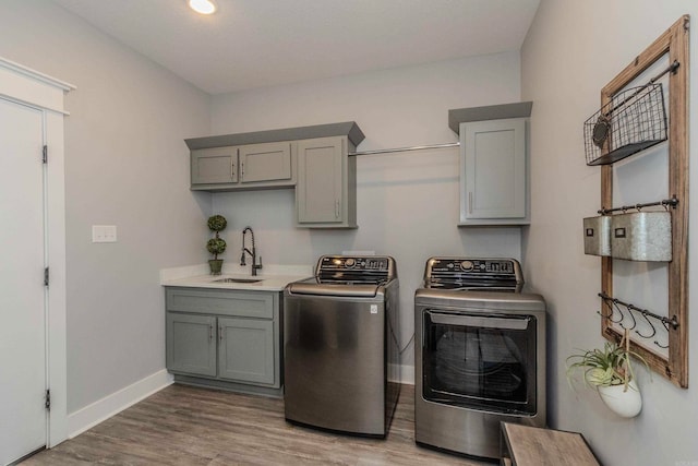 clothes washing area featuring washer and dryer, cabinets, light wood-type flooring, and sink