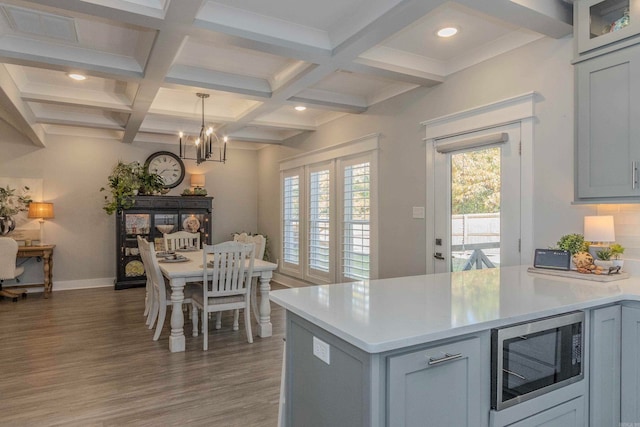 kitchen with decorative light fixtures, hardwood / wood-style flooring, an inviting chandelier, beamed ceiling, and stainless steel microwave