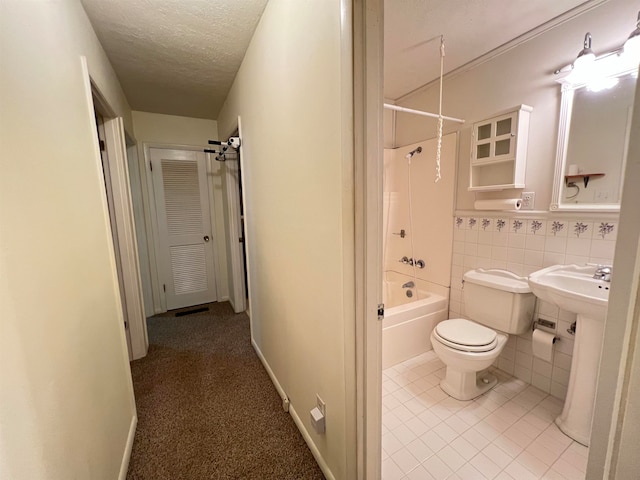 bathroom featuring tile patterned flooring, bathing tub / shower combination, a textured ceiling, toilet, and tile walls