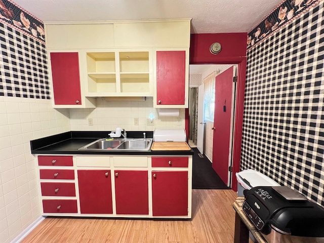 kitchen featuring tile walls, sink, light hardwood / wood-style floors, and a textured ceiling