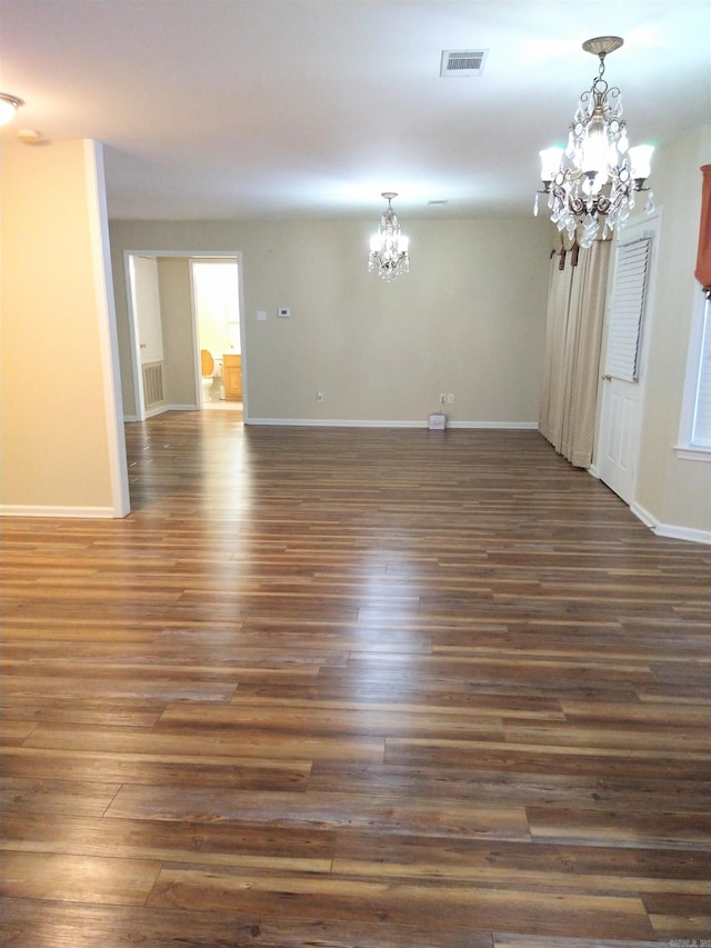 spare room with dark wood-type flooring and an inviting chandelier