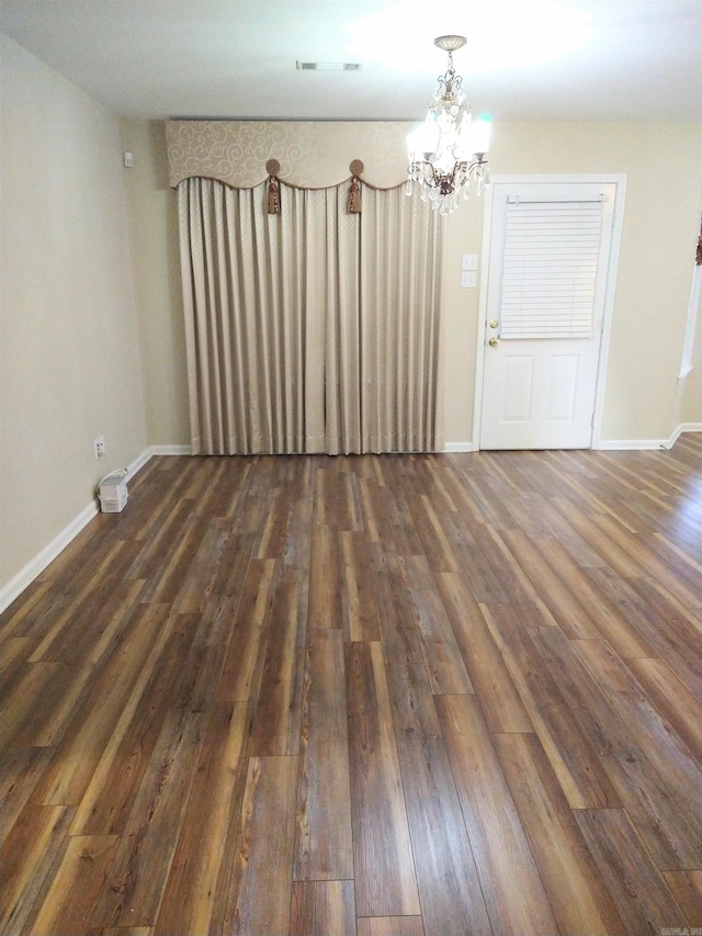 unfurnished room featuring dark wood-type flooring and a notable chandelier