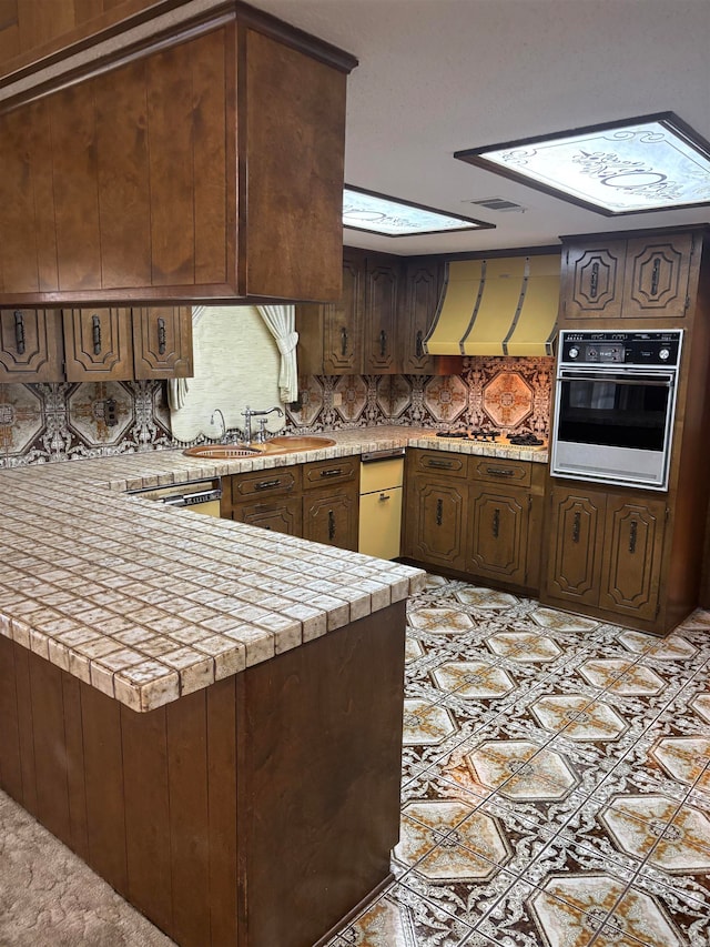 kitchen featuring exhaust hood, sink, kitchen peninsula, black oven, and dark brown cabinets