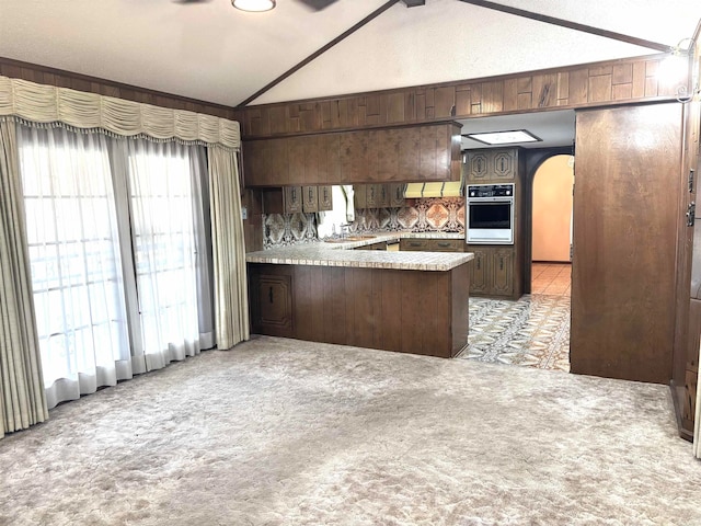 kitchen featuring kitchen peninsula, plenty of natural light, oven, light colored carpet, and vaulted ceiling