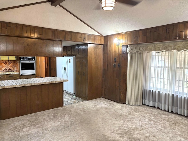 kitchen featuring lofted ceiling with beams, white fridge with ice dispenser, wood walls, and stainless steel oven