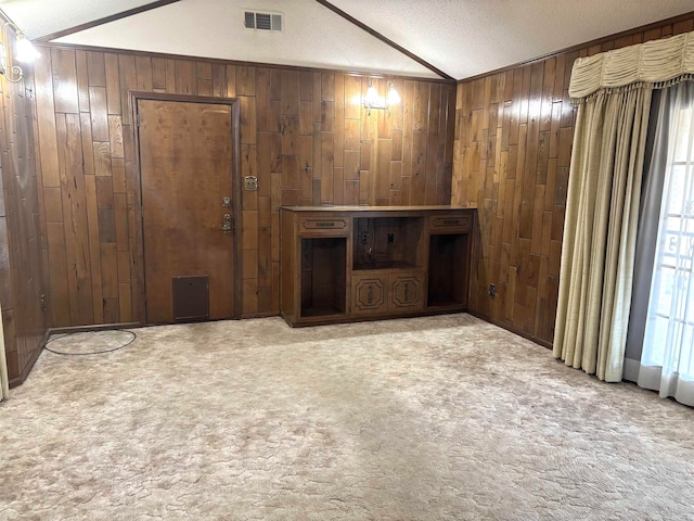 carpeted spare room with vaulted ceiling, wooden walls, and a textured ceiling