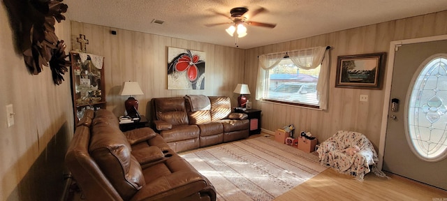 living room featuring ceiling fan, wooden walls, a textured ceiling, and light wood-type flooring