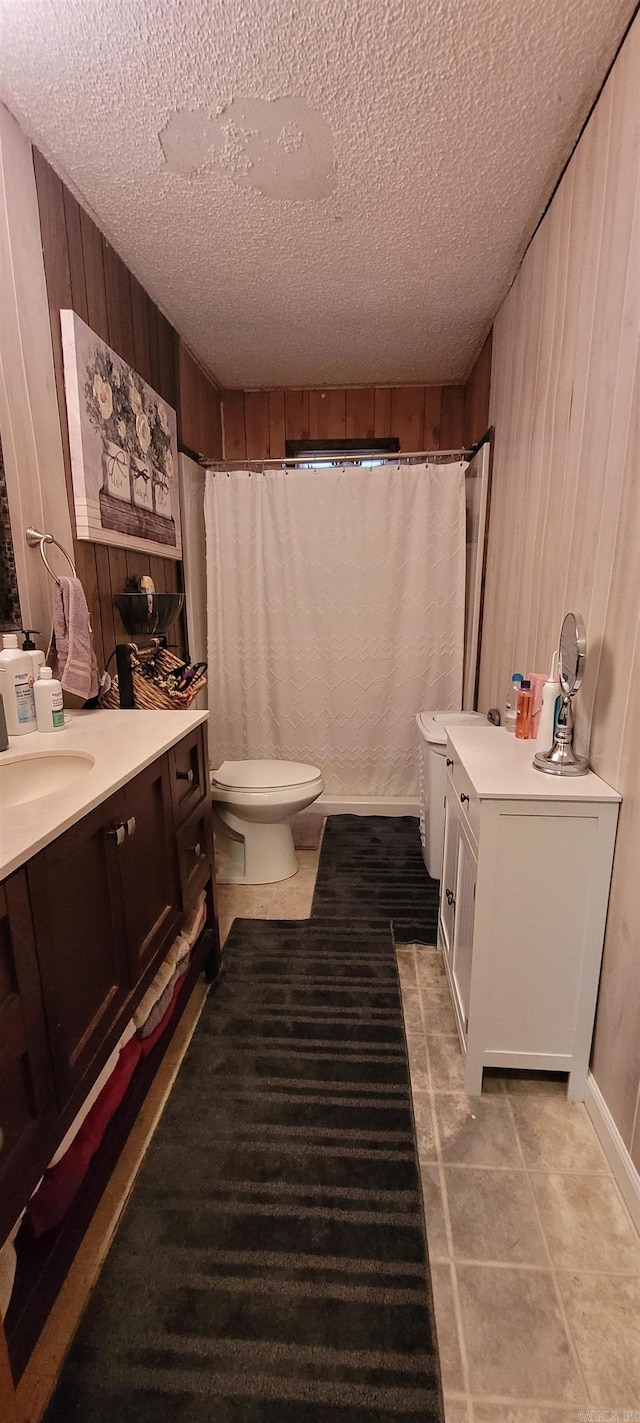 bathroom with vanity, toilet, a textured ceiling, and wooden walls