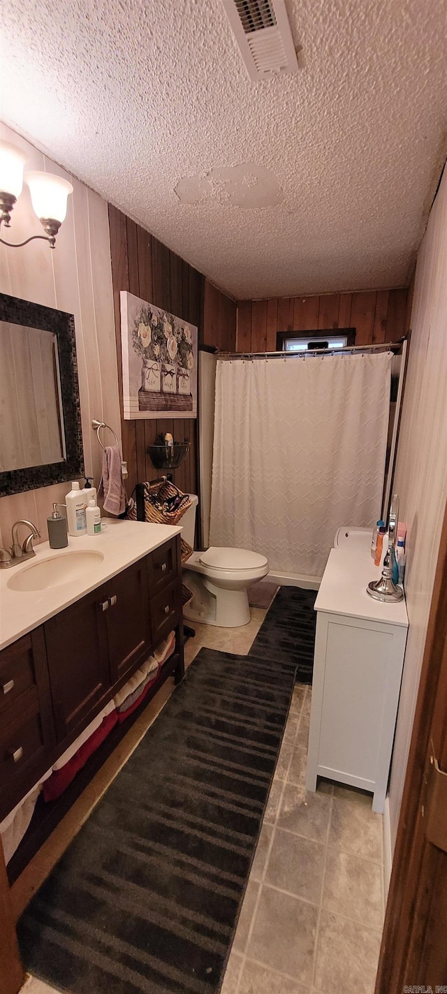 bathroom featuring vanity, wood walls, tile patterned flooring, toilet, and a textured ceiling