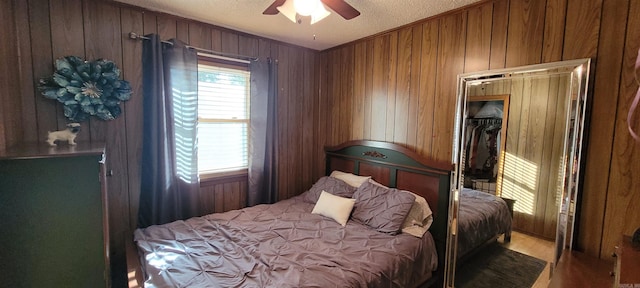 bedroom with a textured ceiling, ceiling fan, wood-type flooring, a closet, and wood walls