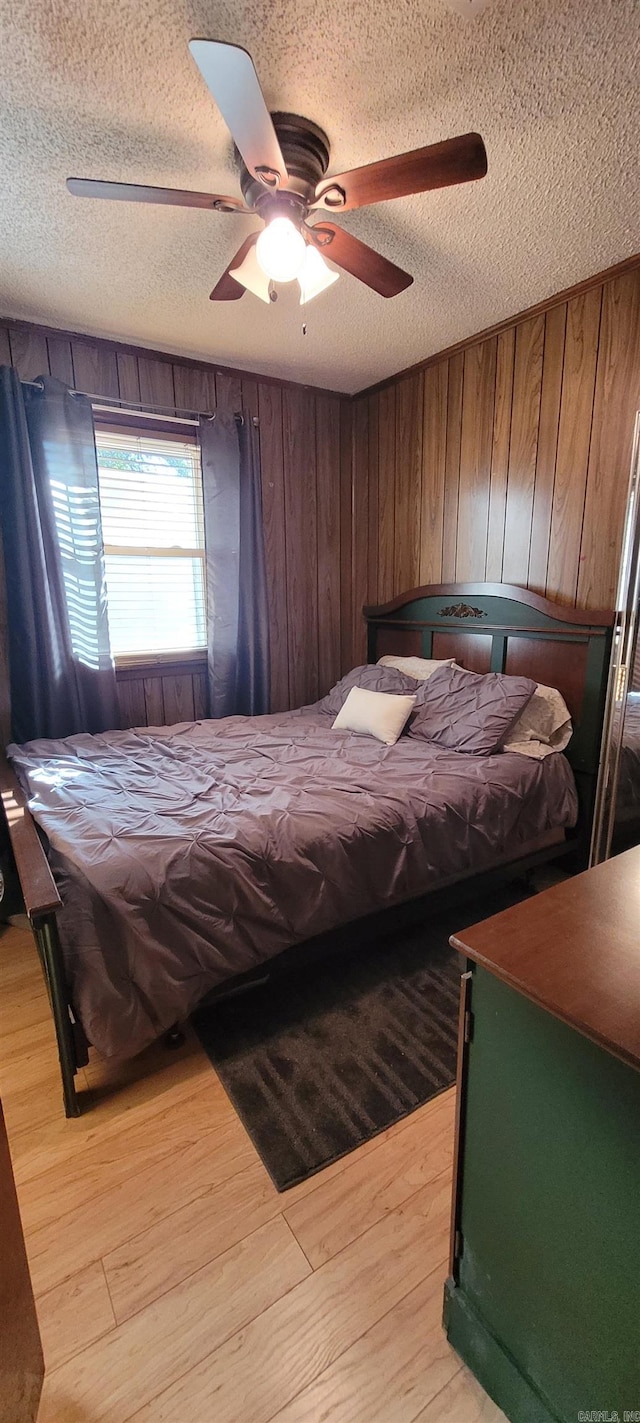 bedroom with ceiling fan, a textured ceiling, wooden walls, and light hardwood / wood-style flooring