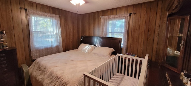 bedroom with multiple windows, wood walls, ceiling fan, and a textured ceiling