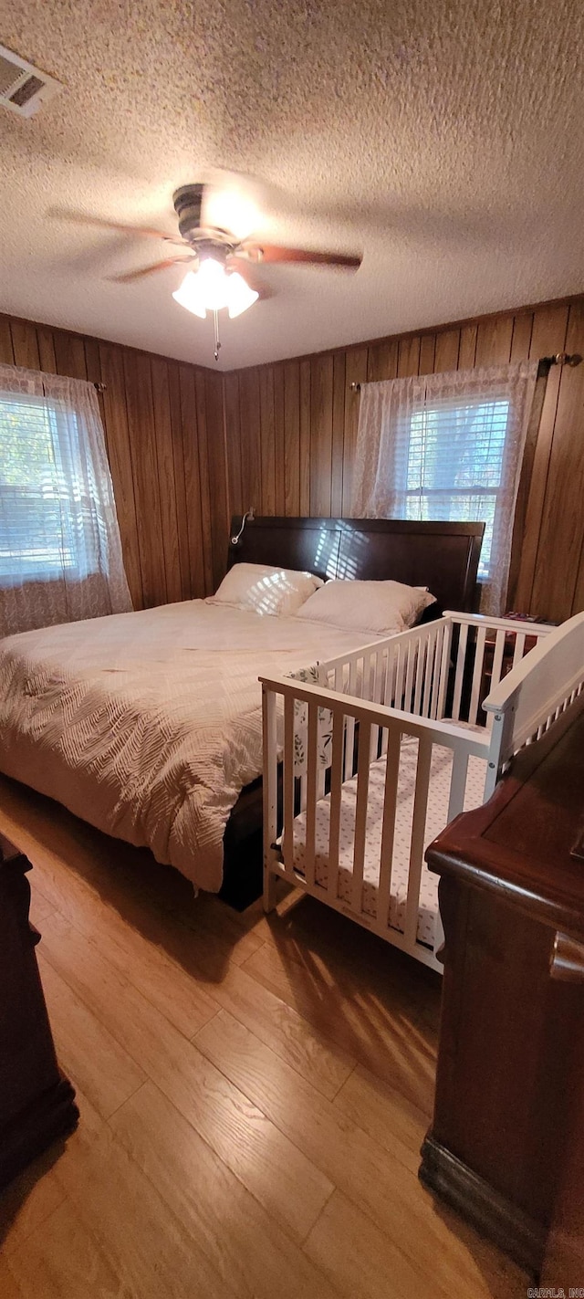 bedroom with hardwood / wood-style flooring, ceiling fan, wood walls, and a textured ceiling