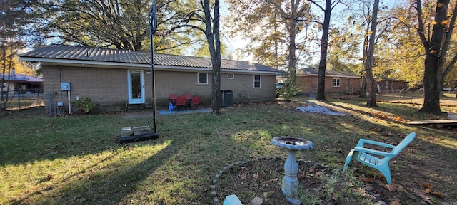 rear view of property featuring a lawn, central air condition unit, and an outdoor fire pit