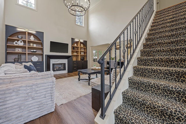 living room featuring hardwood / wood-style floors, a towering ceiling, an inviting chandelier, and built in shelves