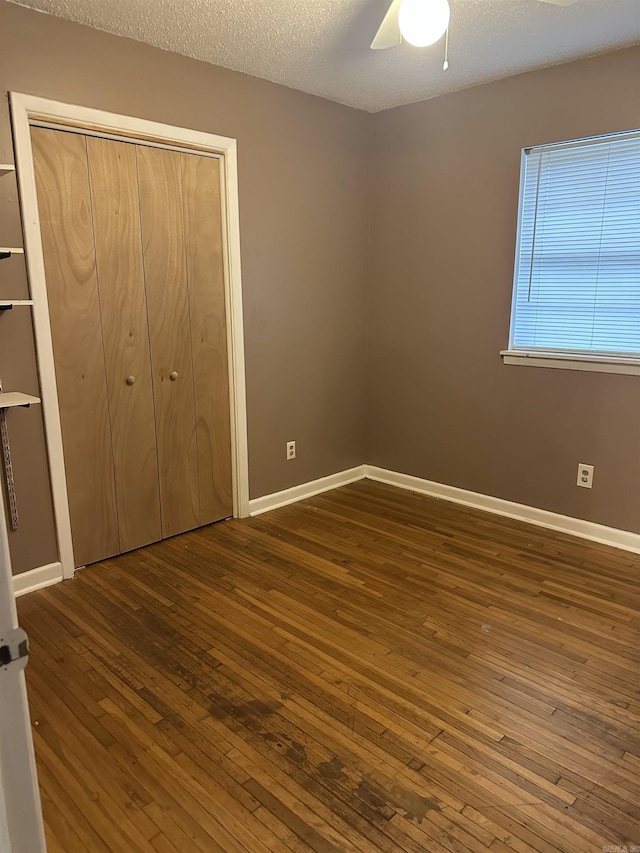 unfurnished bedroom with a textured ceiling, ceiling fan, dark wood-type flooring, and a closet