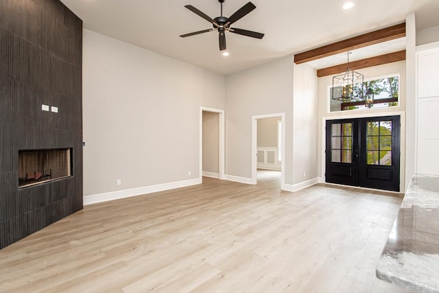 unfurnished living room with beam ceiling, a towering ceiling, light hardwood / wood-style flooring, and french doors