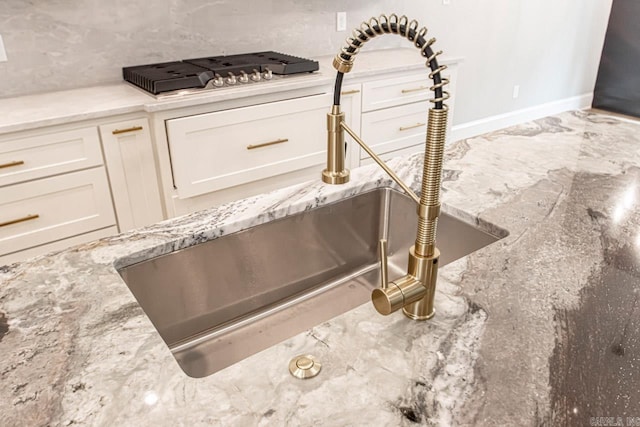 interior details featuring light stone counters, white cabinetry, sink, and gas cooktop