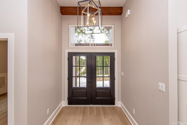 entryway with beam ceiling, french doors, an inviting chandelier, light hardwood / wood-style flooring, and a towering ceiling