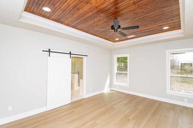 spare room featuring a barn door, light wood-type flooring, and a tray ceiling