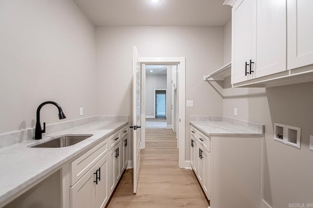 clothes washing area with cabinets, sink, washer hookup, and light hardwood / wood-style flooring