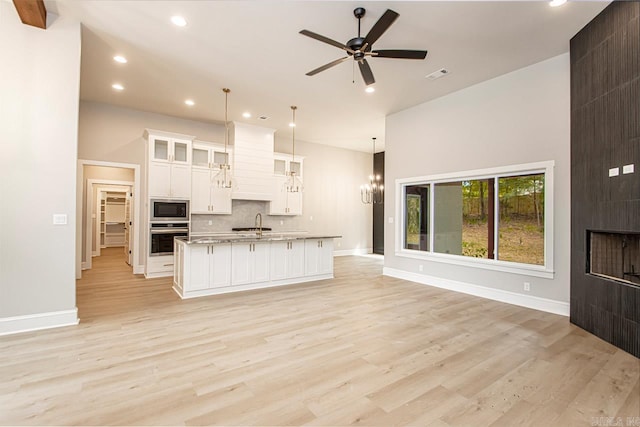 kitchen featuring decorative light fixtures, light wood-type flooring, stainless steel appliances, and a kitchen island with sink