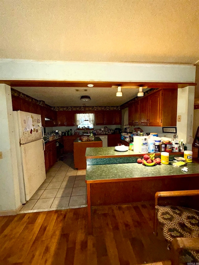 kitchen featuring kitchen peninsula, a textured ceiling, light wood-type flooring, and white fridge