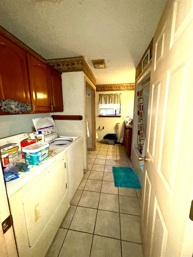 laundry area featuring washing machine and clothes dryer, light tile patterned flooring, cabinets, and a textured ceiling