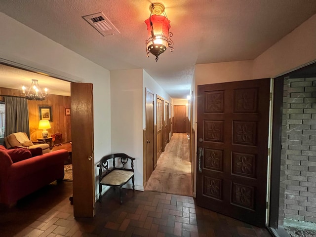 hall with a textured ceiling, wooden walls, and an inviting chandelier