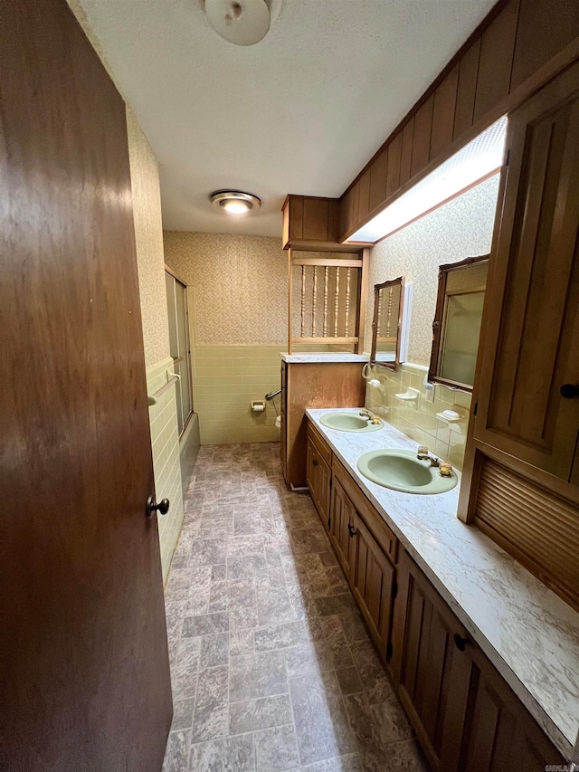 bathroom with vanity, tile walls, and bath / shower combo with glass door