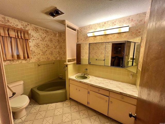 bathroom with vanity, toilet, a textured ceiling, and tile walls