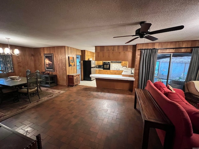 interior space with stainless steel fridge, ceiling fan with notable chandelier, a textured ceiling, and wood walls