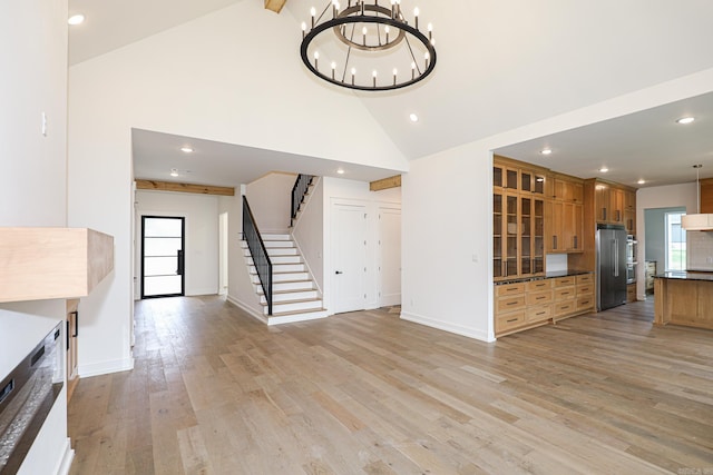 unfurnished living room with an inviting chandelier, high vaulted ceiling, and light wood-type flooring