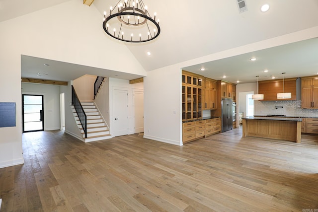 unfurnished living room with high vaulted ceiling, light hardwood / wood-style flooring, and a notable chandelier