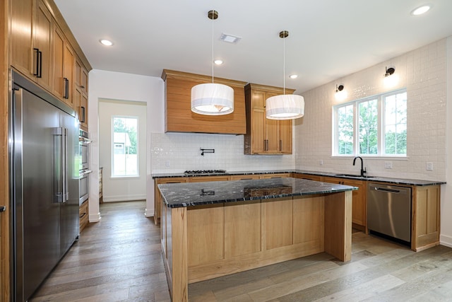 kitchen with appliances with stainless steel finishes, light wood-type flooring, a kitchen island, and pendant lighting