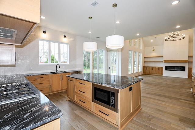 kitchen with pendant lighting, dark stone countertops, a center island, light hardwood / wood-style floors, and stainless steel microwave