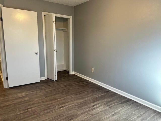 unfurnished bedroom with a textured ceiling, a closet, and dark wood-type flooring