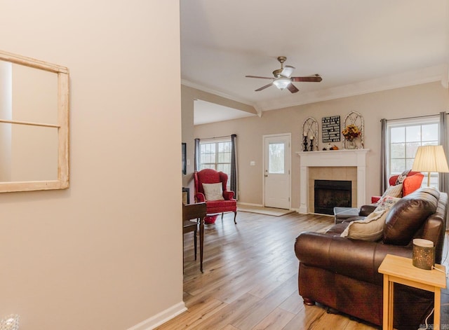 living room featuring light hardwood / wood-style floors, a tile fireplace, ornamental molding, and a wealth of natural light