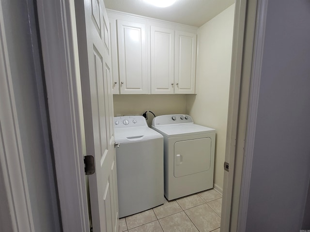 washroom with washing machine and dryer, light tile patterned floors, and cabinets