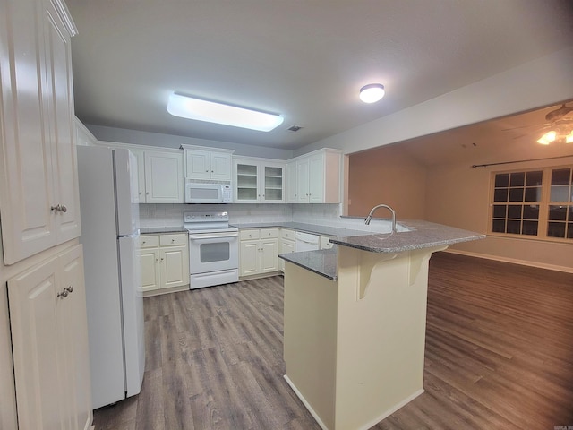 kitchen featuring white appliances, white cabinetry, light hardwood / wood-style floors, kitchen peninsula, and a breakfast bar area