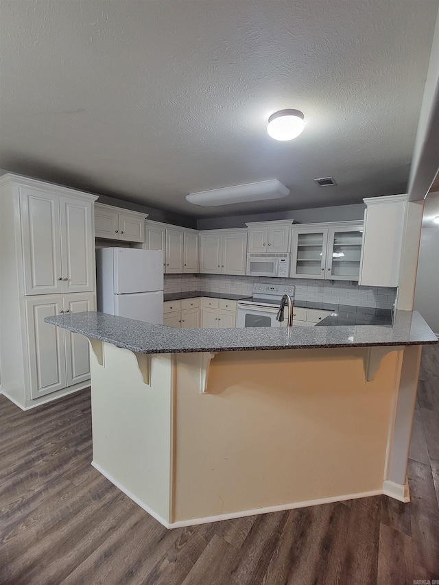 kitchen with white cabinetry, tasteful backsplash, dark hardwood / wood-style flooring, white appliances, and a kitchen bar