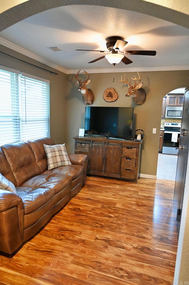 living room with a textured ceiling, light hardwood / wood-style flooring, ceiling fan, and ornamental molding