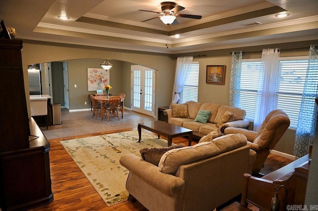 living room with a tray ceiling, french doors, wood-type flooring, and ornamental molding