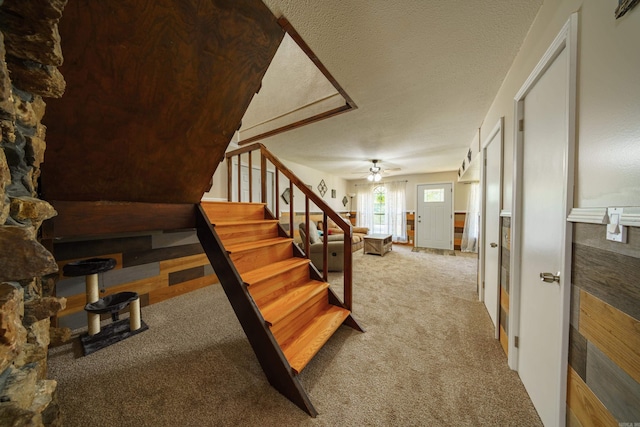 stairs with ceiling fan, carpet floors, and a textured ceiling