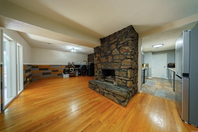 living room with a textured ceiling, light hardwood / wood-style floors, and a stone fireplace