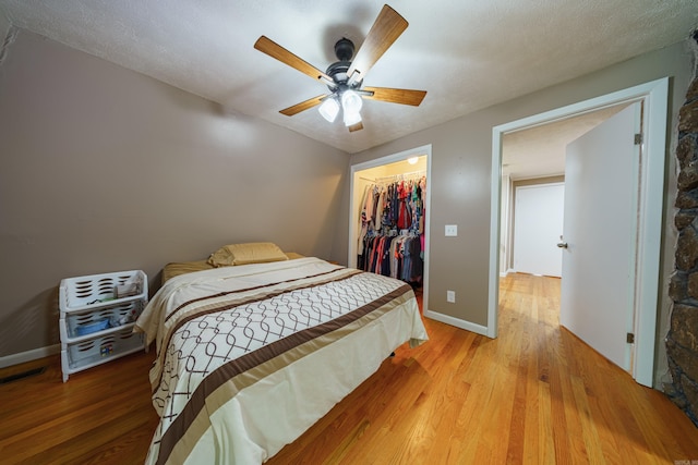 bedroom with a walk in closet, a textured ceiling, ceiling fan, light hardwood / wood-style floors, and a closet